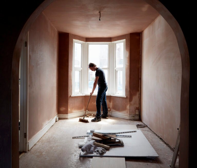 A builder sweeping and tidying up in a renovated replastered house with an archway.
