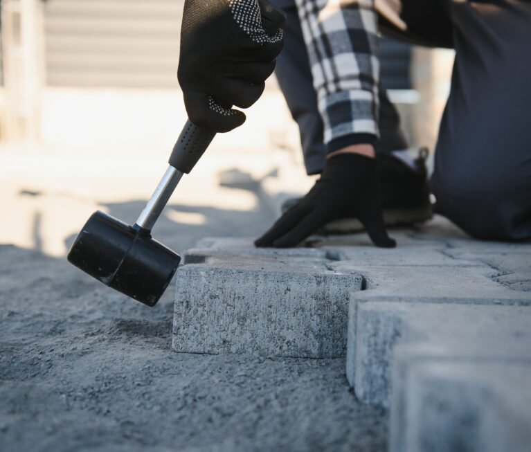 Close-up of construction worker installing and laying pavement stones on terrace, road or sidewalk. Worker using stones and rubber hammer to build stone sidewalk.