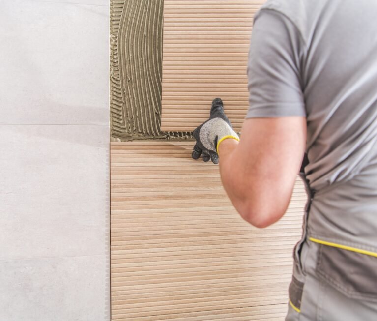 Caucasian Worker Installing Modern Bathroom Tiles. Closeup Photo.