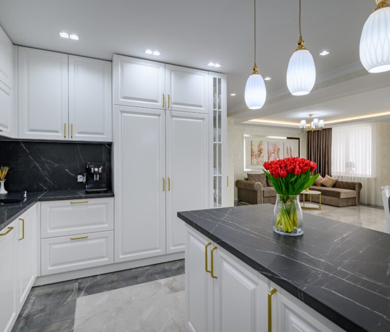 Large black and white expensive well-designed modern kitchen in studio interior, black marble countertop on kitchen island with bouquet of red flowers