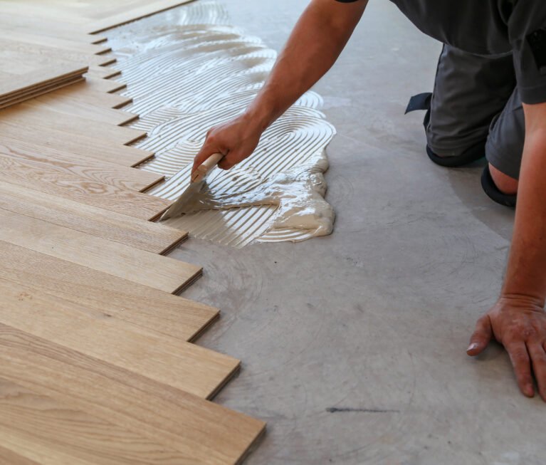 A male worker installing a wooden laminate flooring on his knees