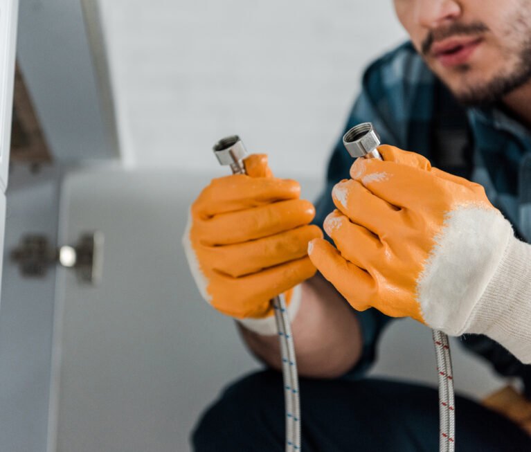 selective focus of handyman holding metal hose near kitchen cabinet