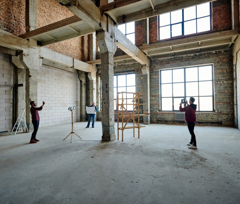 Two young contractors photographing unfinished structure inside building while their colleague looking at sketch on blueprint